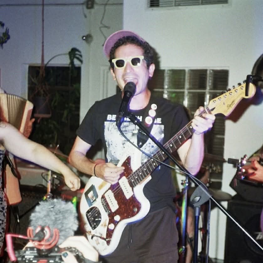 An photo of Jordan C. Weinstock singing and playing guitar.